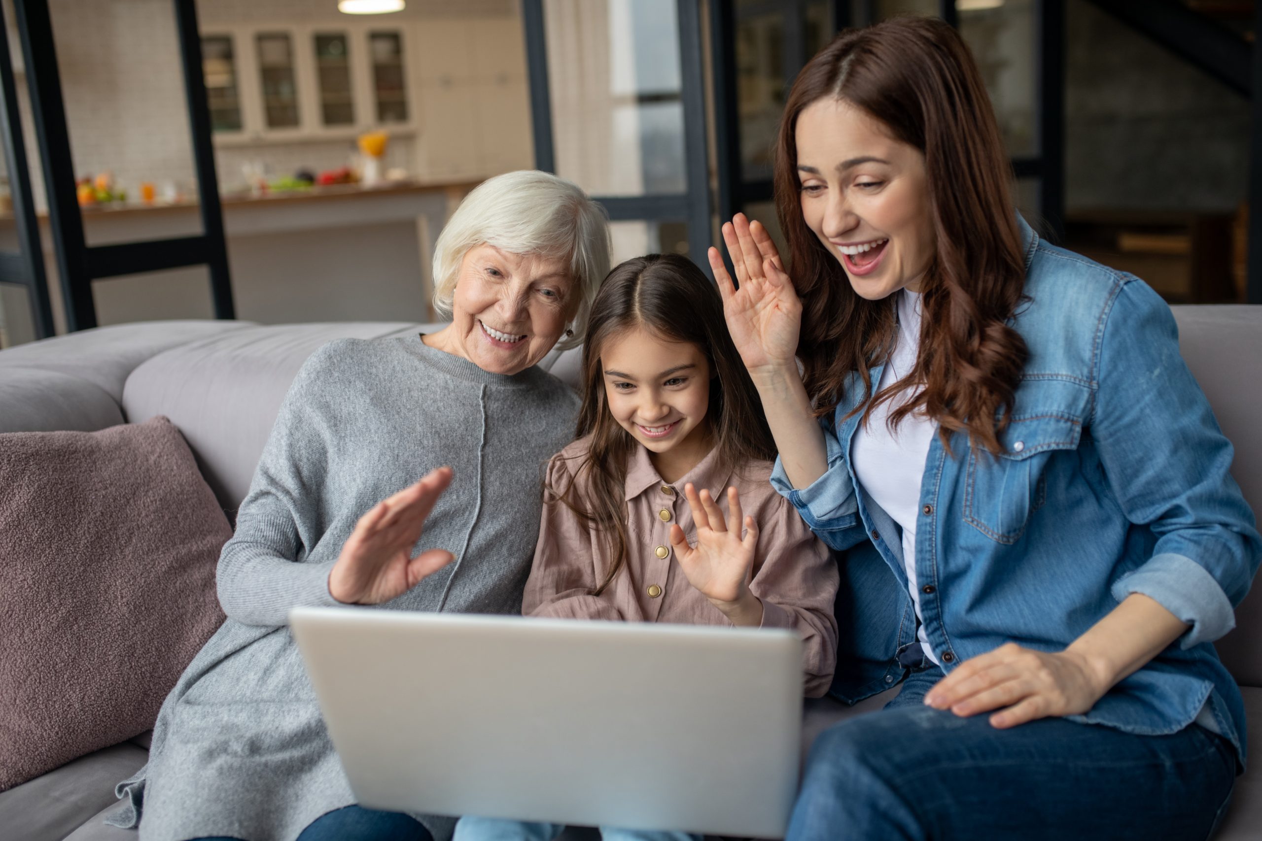 Online call. Daughter her mother and grandmother sitting next to each other on the couch and talking online on the laptop, in a great mood.